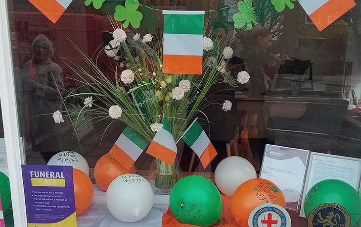 Front shop window decorated for St Patricks Day. With white, green and orange balloons, Irish flags and flowers.